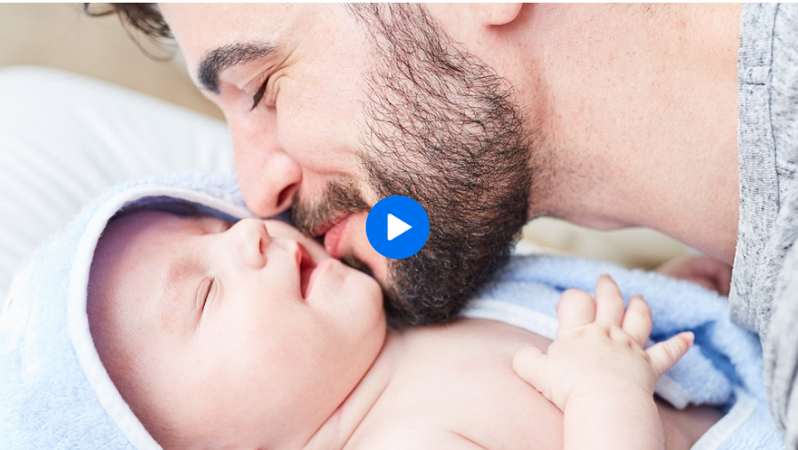Eine als männliche gelesene Person hebt ihr Gesicht fürsorglich an das Kind eines Babies.