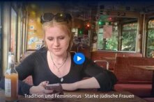 Eine weiblich gelesene Person sitzt an einem Tisch in einem Café und schaut auf ihr Handy.