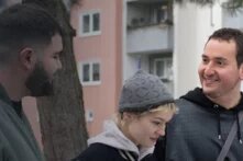 Drei Personen vor einer Häuserreihe, die miteinander reden. 