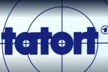 "Tatort" in dunkelblauen Kleinbuchstaben vor weißem Hintergrund. Dunkelblaue dünne Kreise und Linien ähneln einer Schusshilfe bei einem Gewehr. 