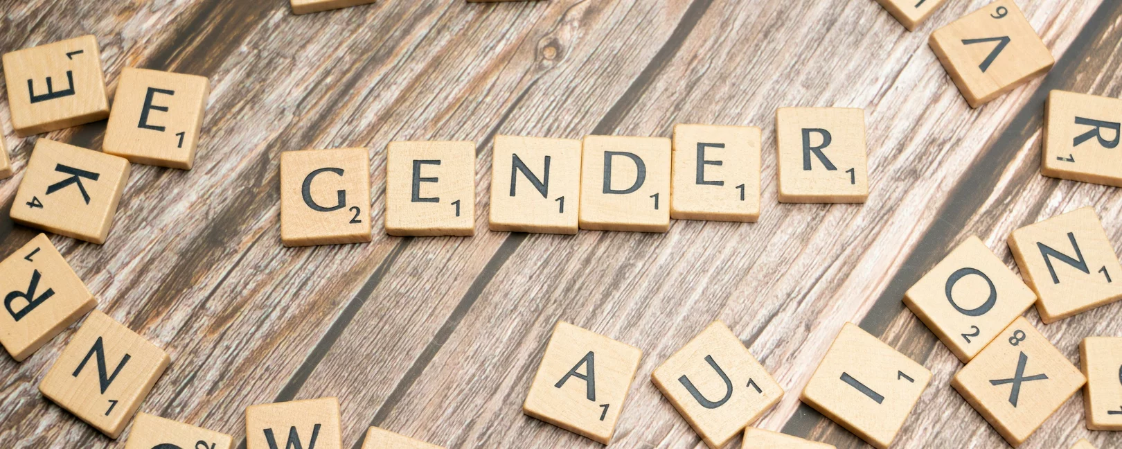 Auf einem Holzuntergrund liegen Scrabble-Buchstabensteine, in der Mitte ist das Wort 