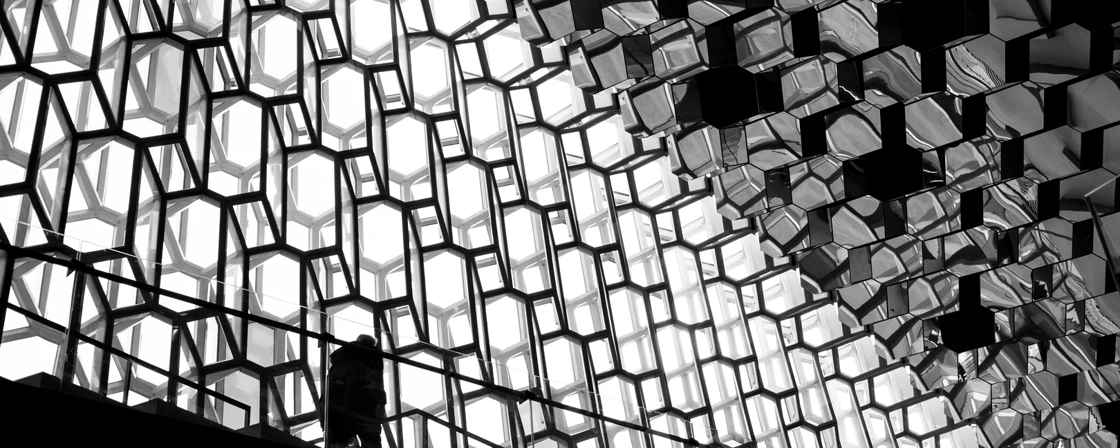 Person die vor einem schwarz weiß grauem Hintergrund aus Gittern eine Treppe hochgeht. 