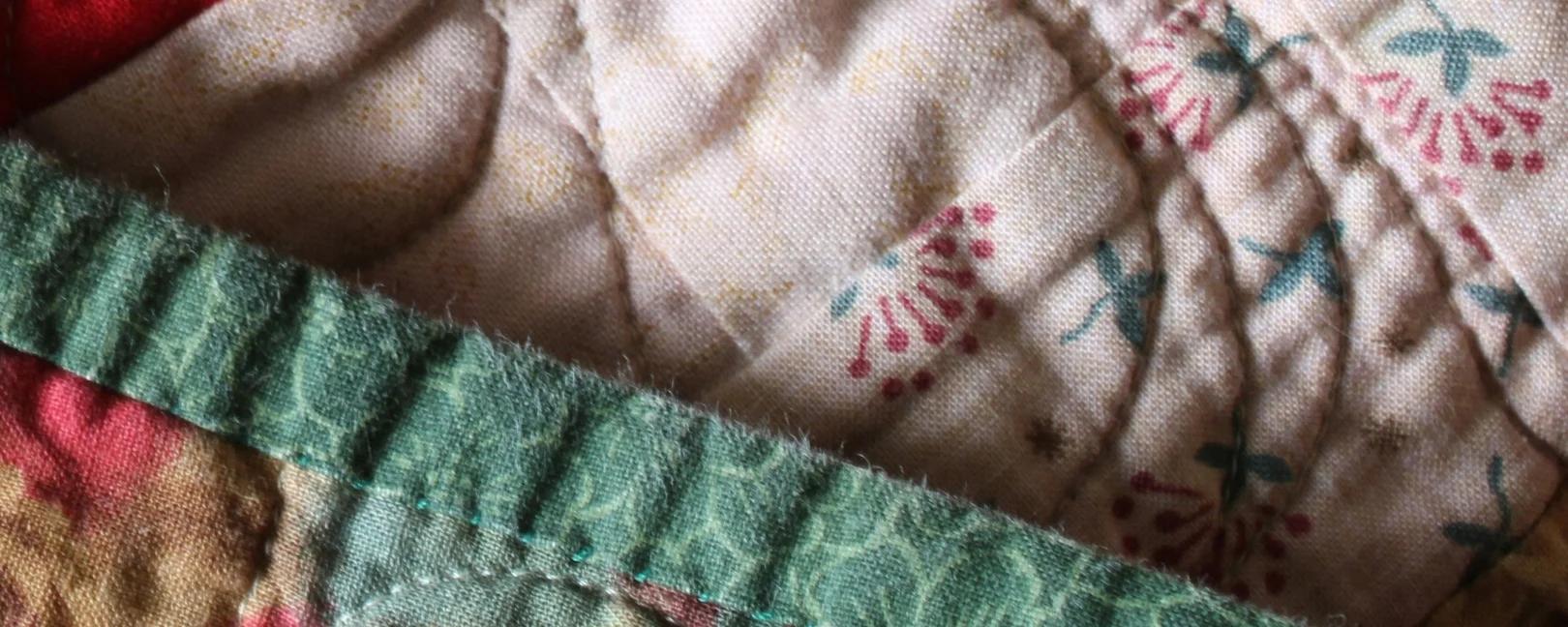 Patchwork-Decke in Pastellfarben mit Stickereien – Symbol für Vielfalt und Fürsorge. Thema: Eltern werden & reproduktive Gerechtigkeit.