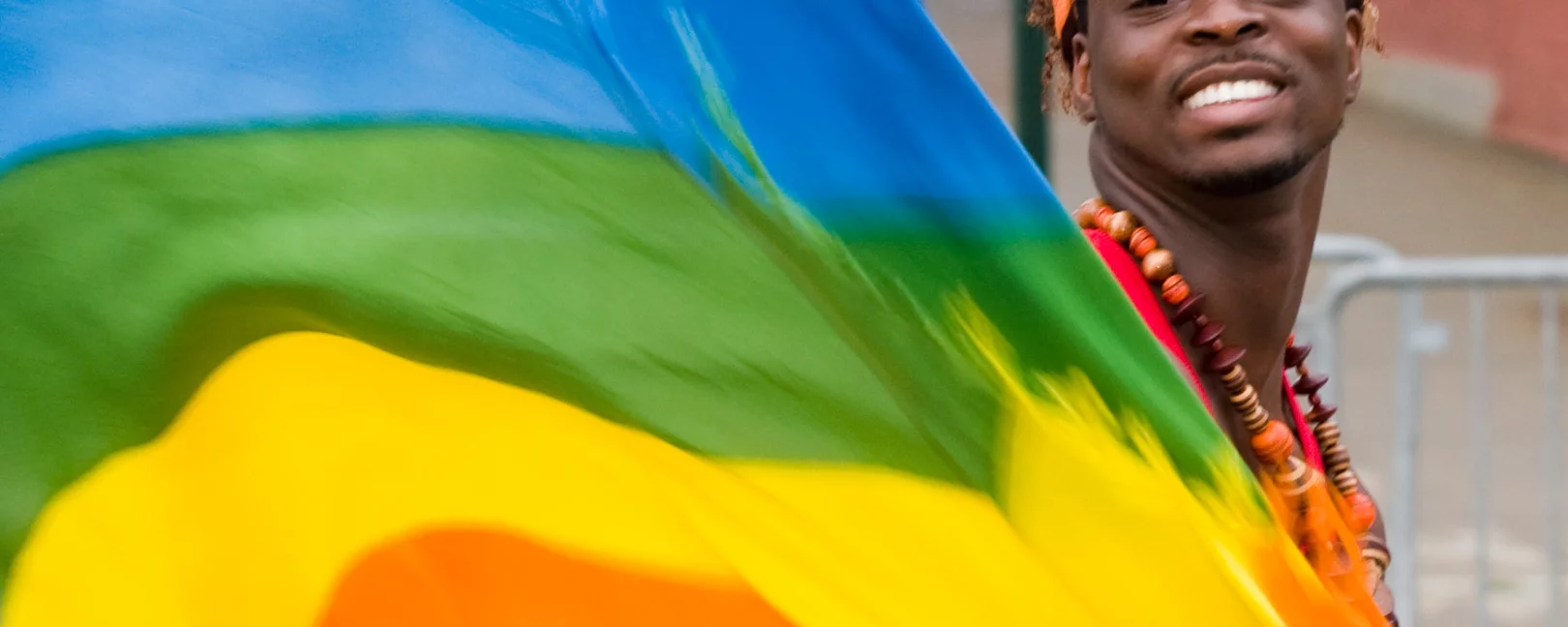 Eine Schwarze Person lächelt in die Kamera und schwingt dabei eine große Regenbogen Flagge.